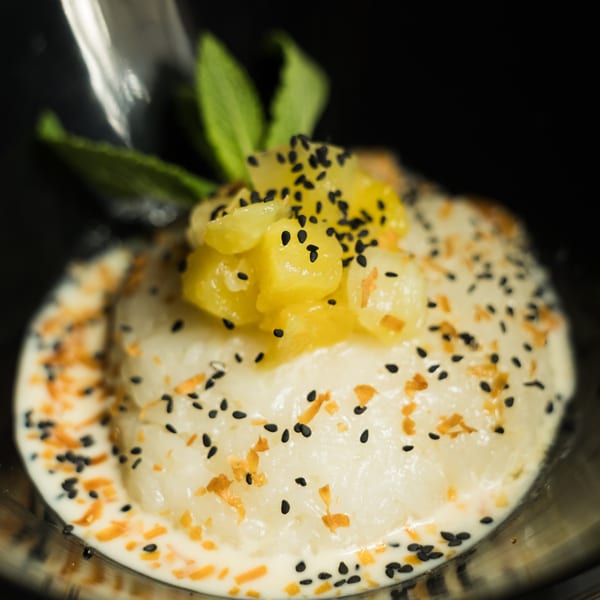 Sweet sticky rice with mango, black sesame seeds, and mint in a dark bowl.