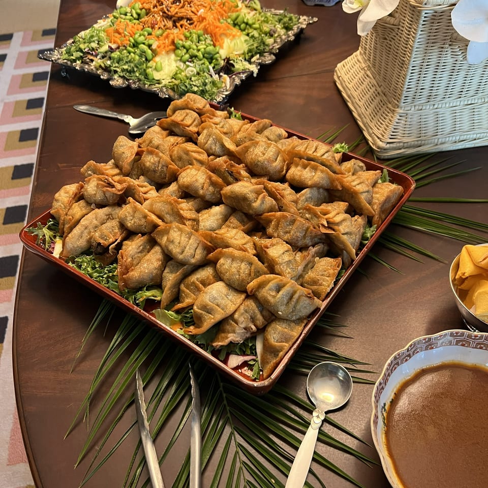 A buffet table with fried dumplings, a colorful salad, and a bowl of dipping sauce.