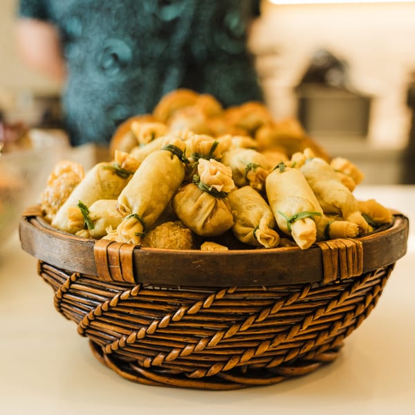 A woven basket filled with golden-fried spring rolls and money bags, garnished with chives.