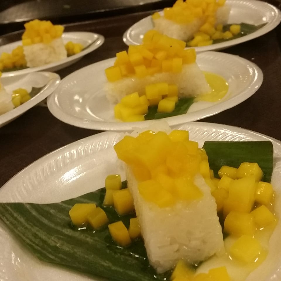 Multiple servings of mango sticky rice on white plates, garnished with green leaves.