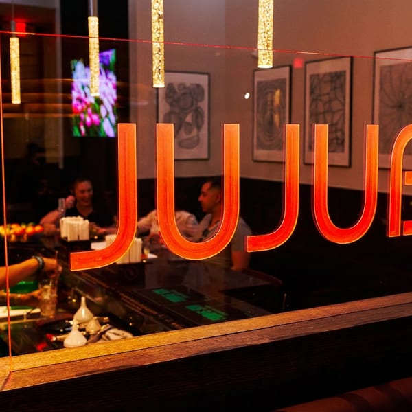 The JujuBe restaurant sign in neon orange, with a bartender and patrons visible in the background.