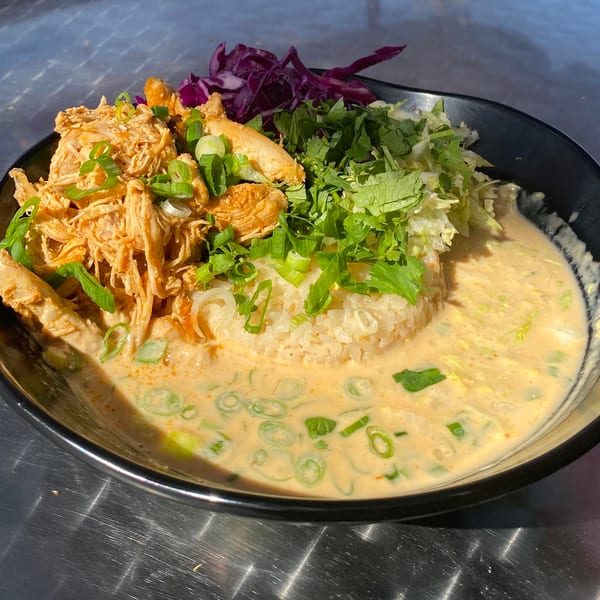 A black bowl filled with shredded chicken, rice, red cabbage, cilantro, and green onions in a creamy sauce.