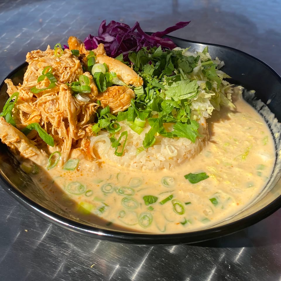 A black bowl filled with shredded chicken, rice, red cabbage, cilantro, and green onions in a creamy sauce.