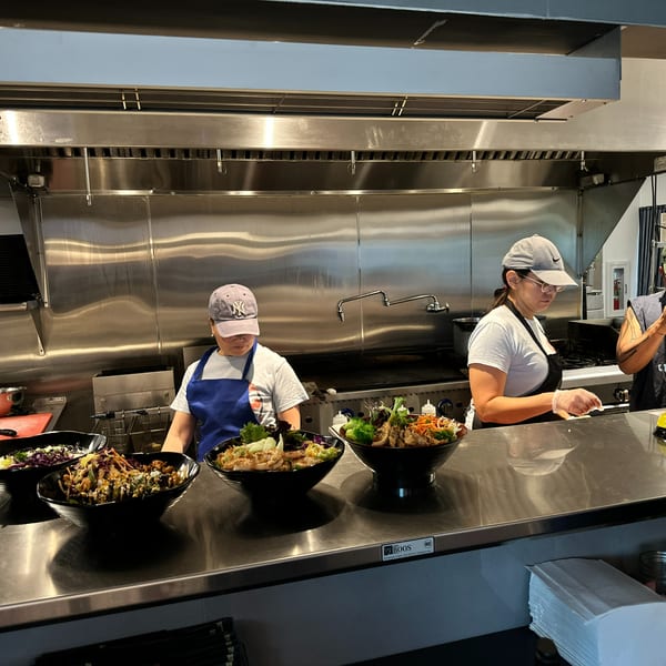 Three restaurant staff members behind a counter with several large bowls of food ready for service.