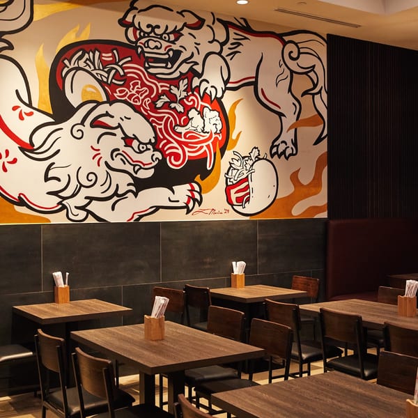 Restaurant interior with wooden tables and chairs, a dark paneled wall, and a large mural of mythical creatures.