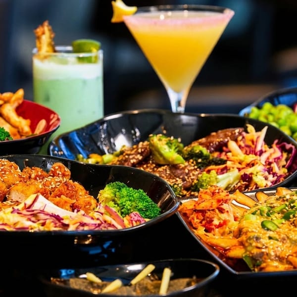 A table laden with various Asian-inspired dishes, including bowls of chicken, beef, salads, and fries.