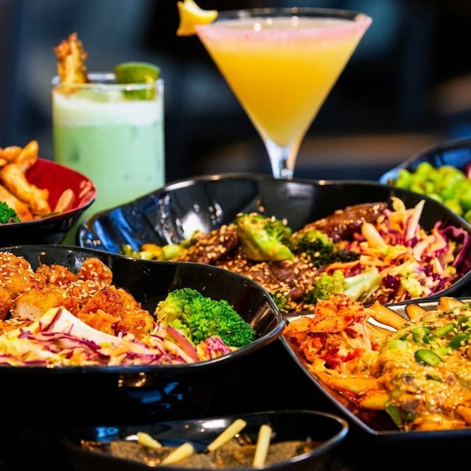 A table laden with various Asian-inspired dishes, including bowls of chicken, beef, salads, and fries.