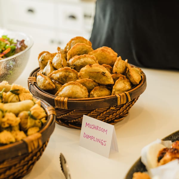 Baskets of mushroom dumplings and other appetizers on a white table with a salad in the background.