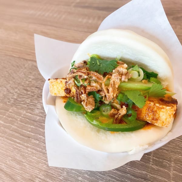 Steamed bao bun filled with tofu, green peppers, cilantro, and crispy fried onions on a wooden table.
