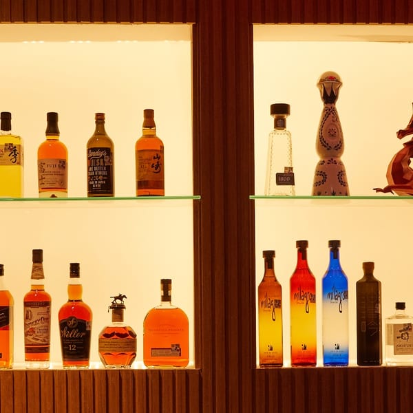 A backlit liquor display with various bottles of whiskey, tequila, and other spirits on glass shelves.
