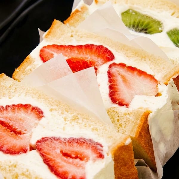 Rows of fruit sandwiches with strawberries and kiwi slices, cream, and white bread.