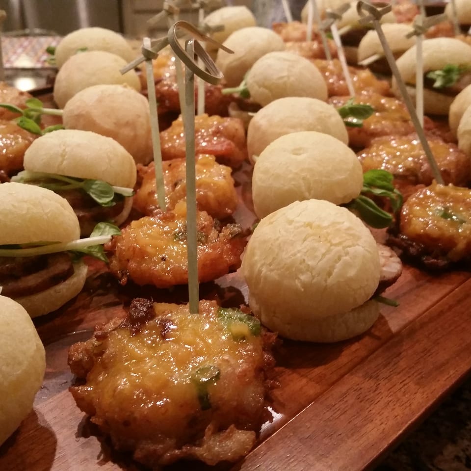 Mini sliders and fried appetizers with toothpicks arranged on a wooden serving tray.