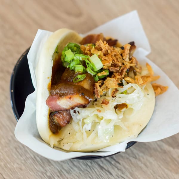 A bao bun filled with pork belly, sauce, fried onions, and green onions on a wooden table.