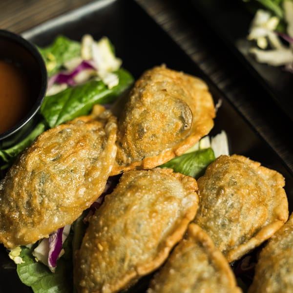 Golden-brown fried dumplings, served on a bed of fresh green and purple lettuce with a side of dipping sauce.